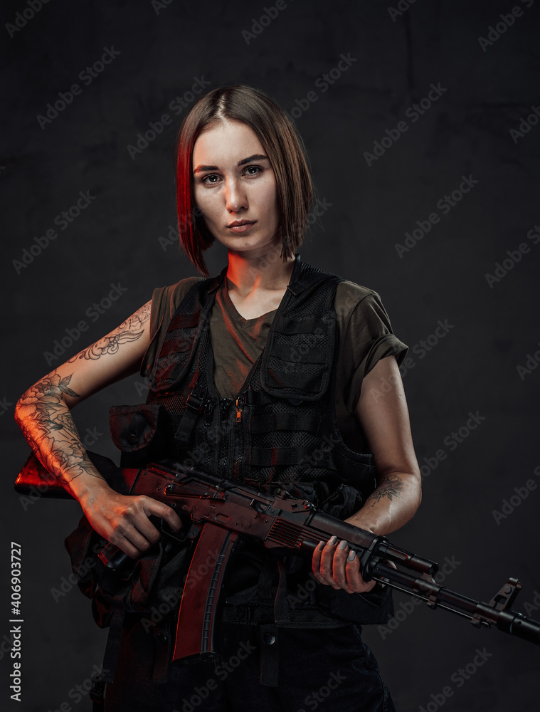Dressed in black armour with dark shirt martial woman with short haircut poses in dark background holding assault rifle. Dressed in black armour with dark shirt martial woman with short haircut poses in dark background holding assault rifle.