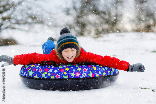 Active school boy sliding down the hill on snow tube. Cute happy child having fun outdoors in winter on sledge . Healthy excited kid tubing snowy downhill, action on family winter time. photo