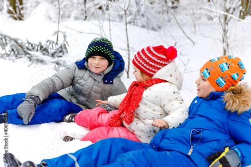 Two school kid boy and little toddler girl in winter forest. Happy children having fun with snow outdoors in winter. Family, three siblings, sister and brothers together, outdoors. Active leisure photo