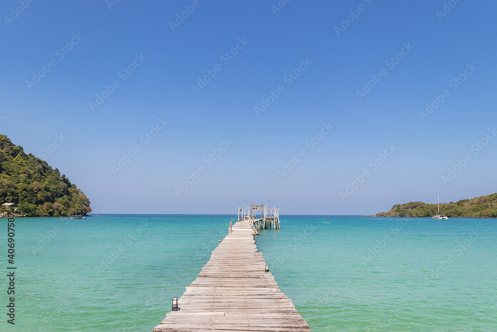 wooden bridge extended into the tropical seascape with beautiful  clear blue sky.