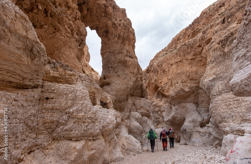 Hikers on a hiking trail inside a deep dry canyon in a remote desert region. High white walls of a narrow canyon, rock formations of unusual shapes. Rock arch inside a canyon.