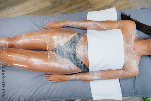 A young beautiful girl is doing a cosmetology procedure full body wrap in a modern beauty salon. Spa procedures in a beauty salon