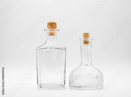 Empty glass carafe and empty glass bottle closed with cork caps isolated on a white background. Pair of the transparent bottles. Front view of the two vertical staying jars with different shape.