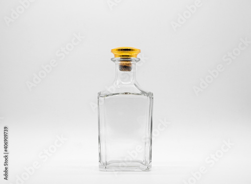 Empty glass bottle closed with big golden round cork isolated on a white background. Transparent square bottle. Front view of the vertical staying jar.
