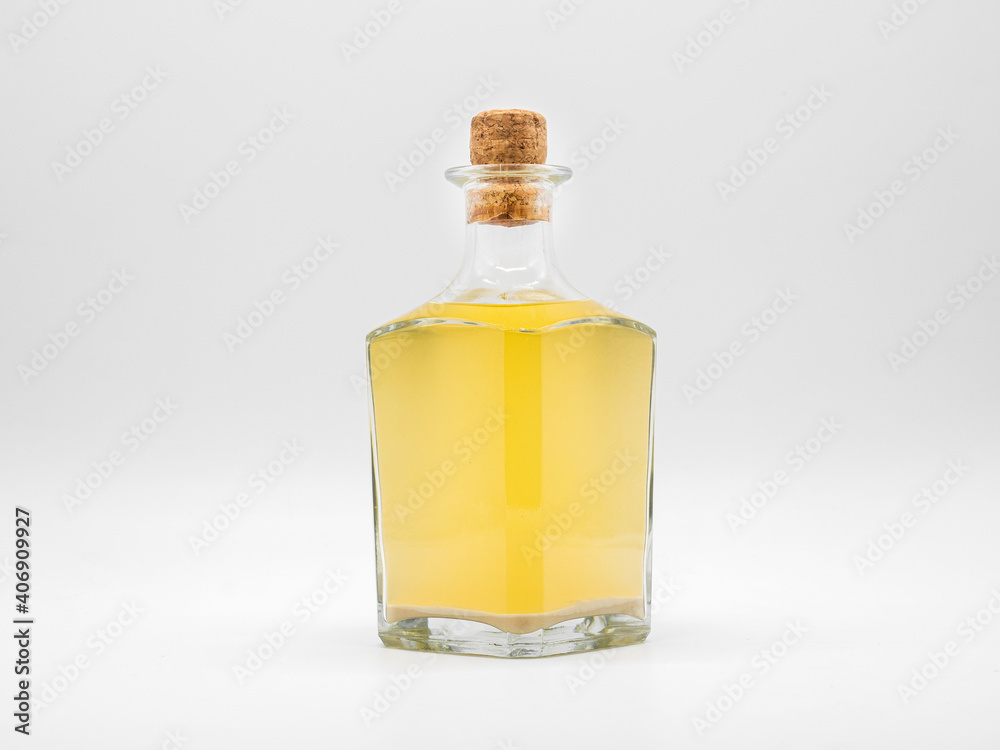 Glass bottle with alcohol drink closed with cork cap isolated on a white background. Transparent square bottle with yellow liquid. Front view of the vertical staying jar.