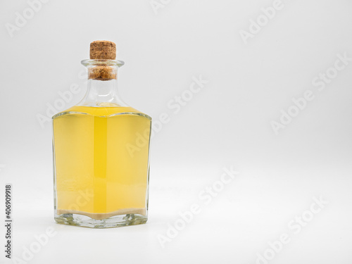Glass bottle with alcohol drink closed with cork cap isolated on a white background. Transparent square bottle with yellow liquid. Front view of the vertical staying jar.