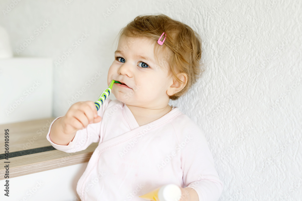 Little baby girl holding toothbrush and brushing first teeth. Toddler learning to clean milk tooth. Prevention, hygiene and healthcare concept. Happy child in bathroom Little baby girl holding toothbrush and brushing first teeth. Toddler learning to clean milk tooth. Prevention, hygiene and healthcare concept. Happy child in bathroom