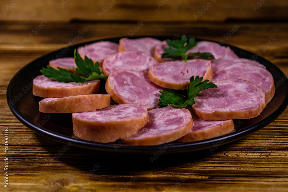 Black plate with sliced sausage on a wooden table