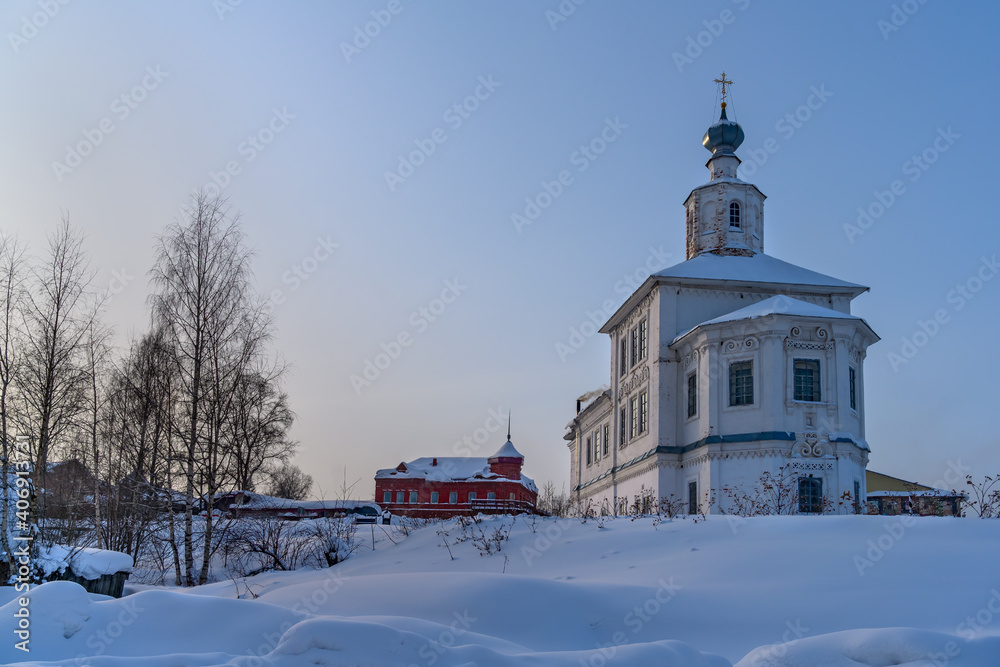 old church in the snow. winter in Cherdyn (Northern Urals, Russia). rich decoration with stucco, curls. at the top of the turret. bright hues. thick layer of snow on the ground blue sky, sunny day
