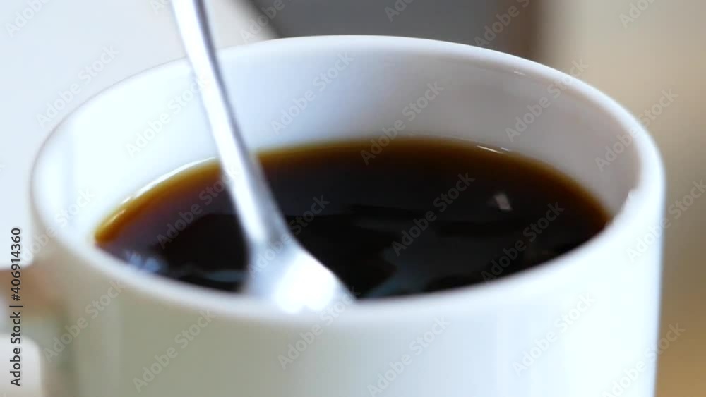 Close-up of Hand stirring sugar in a cup of aromatic coffee with spoon. A cup of aromatic coffee is placed on a wooden table. Close-up of Hand stirring sugar in a cup of aromatic coffee with spoon. A cup of aromatic coffee is placed on a wooden table.