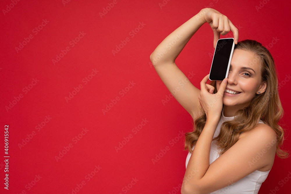 Naklejka premium Photo of beautiful smiling young woman good looking wearing casual stylish outfit standing isolated on background with copy space holding smartphone showing phone in hand with empty screen display for