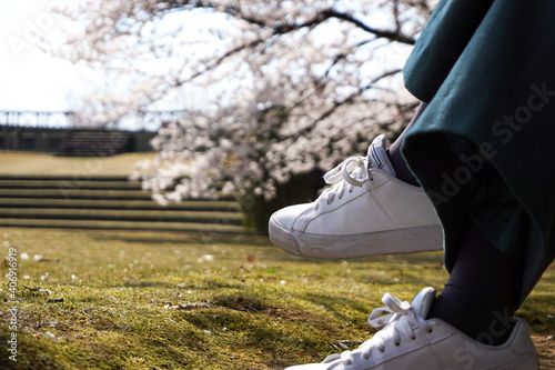 A person sitting in a park where cherry blossoms are in bloom.  桜が咲く公園で座っている人の足。