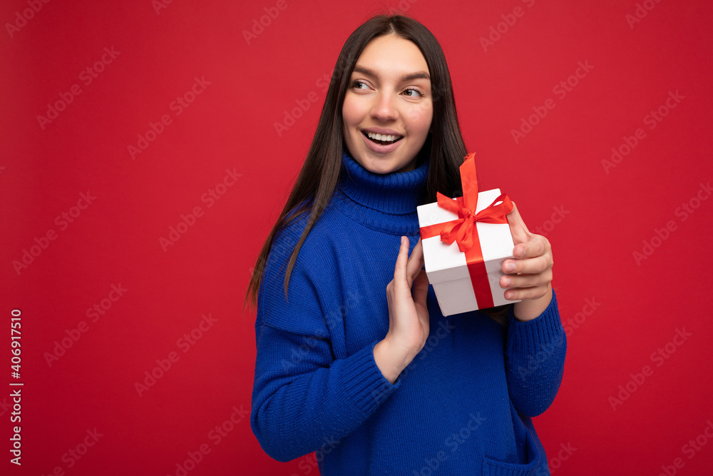 Beautiful happy young brunette woman isolated over colourful background wall wearing stylish casual clothes holding gift box and looking to the side Beautiful happy young brunette woman isolated over colourful background wall wearing stylish casual clothes holding gift box and looking to the side