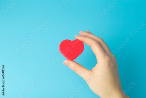 Heart in the hands of a female on a colored background. Donation, charity, health treatment, help concept. Background for Valentine's Day (February 14) and love.