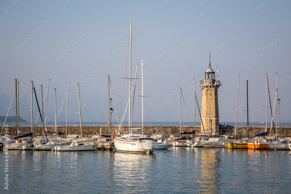 A bay with a marina and the ancient lighthouse of Desenzano del Garda. Early autumn evening. Lombardy, Italy