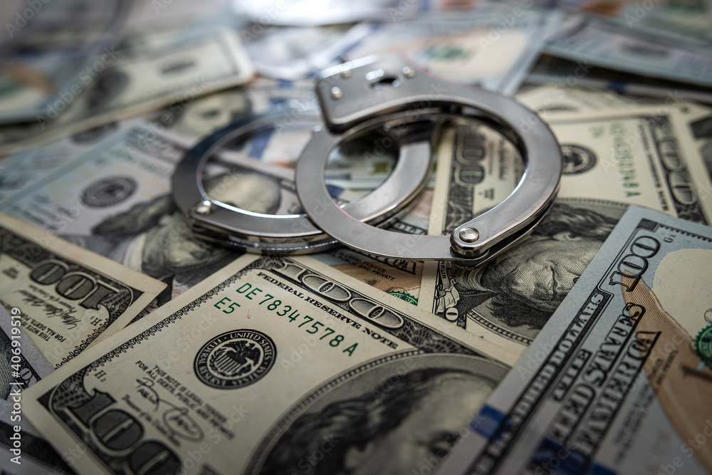 close up of metal handcuffs on hundred dollar banknotes close up of metal handcuffs on hundred dollar banknotes