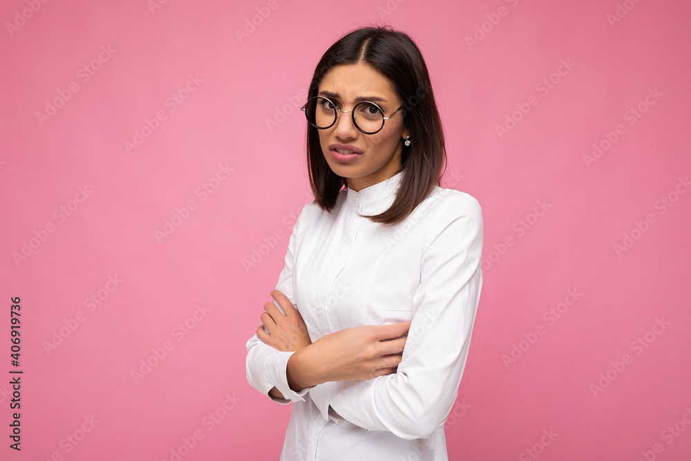 Shot of pretty dissatisfied angry offended young brunette woman wearing white shirt and stylish optical glasses isolated over pink background looking at camera Shot of pretty dissatisfied angry offended young brunette woman wearing white shirt and stylish optical glasses isolated over pink background looking at camera