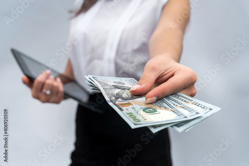 successful business woman holding dollar bills and using tablet isolated grey background.