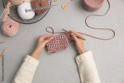 Woman crocheting with threads at grey table, top view. Engaging hobby photo