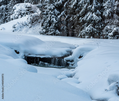 Winter scenery with creek with lot of snow around and trees on the background photo