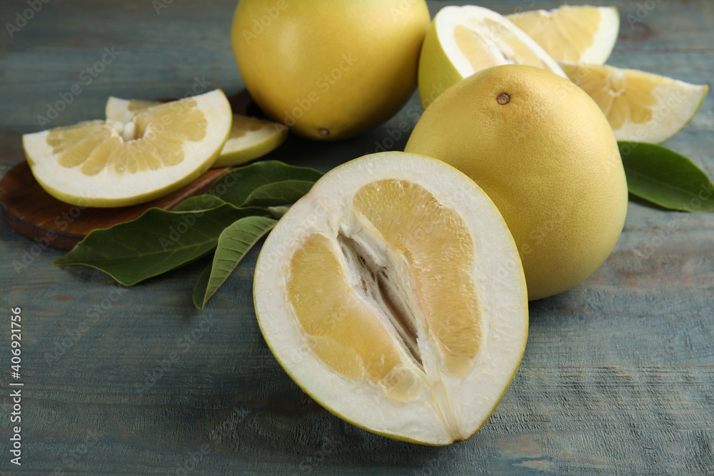 Fresh cut and whole pomelo fruits with leaves on blue wooden table Fresh cut and whole pomelo fruits with leaves on blue wooden table