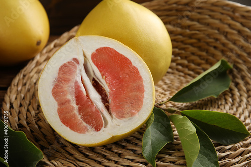 Fresh cut and whole pomelo fruits with leaves on wicker mat, closeup