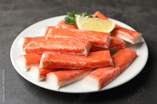 Plate of fresh crab sticks with lemon on grey table, closeup