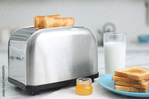 Modern toaster with slices of bread, honey and milk on white table in kitchen
