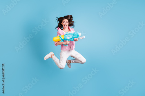 Full length portrait of playful lady jum hold water weapon open mouth wear pants shoes isolated on blue color background