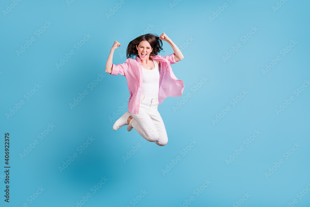 Full size photo of attractive lady jumping fists up celebrate scream open mouth isolated on blue color background Full size photo of attractive lady jumping fists up celebrate scream open mouth isolated on blue color background