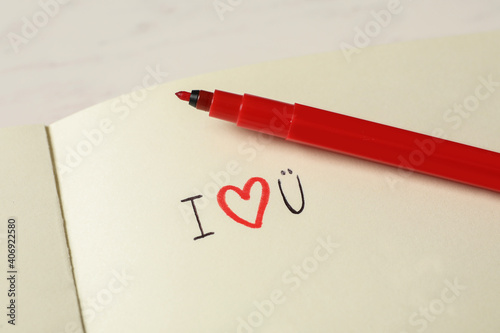 Notebook with text I Love You and red marker on white table, closeup