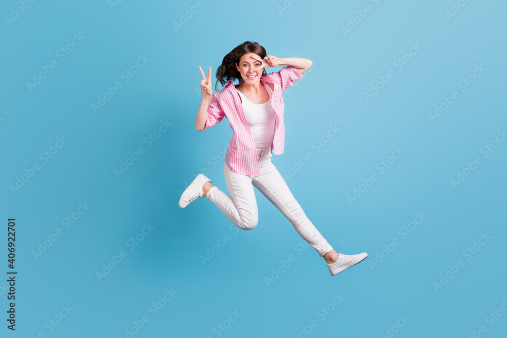 Full body photo of attractive lady jump two hands fingers show v-sign greetings isolated on blue color background Full body photo of attractive lady jump two hands fingers show v-sign greetings isolated on blue color background