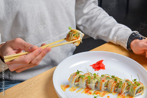 Eating sushi, still life, eating out concept. Young man in restaurant or at home eats Japanese sushi rolls set.