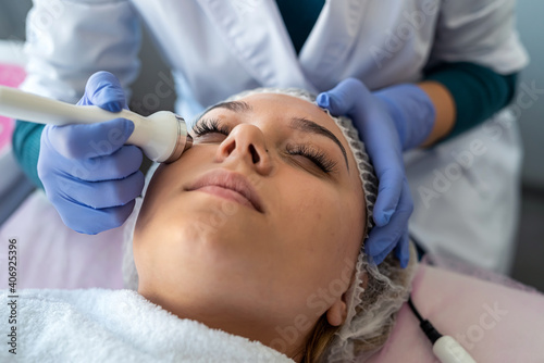 young woman receiving professional procedure facial skin ultrasound cavitation from cosmetologist