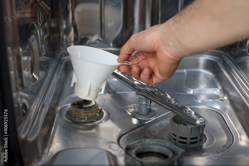 A man inserts a funnel into the hole of the dishwasher to fill it with salt