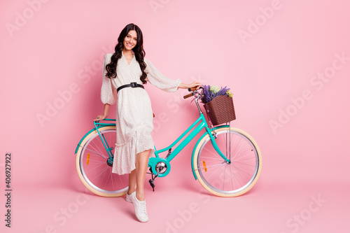 Full length body size photo of pretty girl standing with blue bicycle on holidays isolated on pastel pink color background © deagreez
