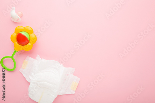 Fototapeta Naklejka Na Ścianę i Meble -  White baby diaper, soother and colorful flower rattle toy on light pink table background. Pastel color. Closeup. Empty place for text. Top down view.