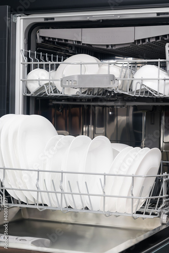 white plates and cups lie in the basket of the dishwasher