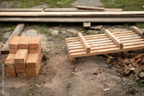 On the ground is a pile of new bricks  pine boards. Preparing material for the rack