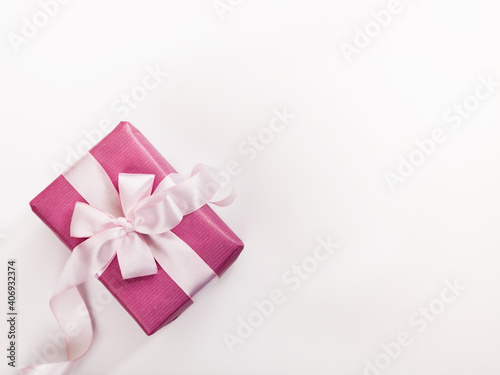 Pink gift box, white bow, curved ribbon and empty space for text on white background.
