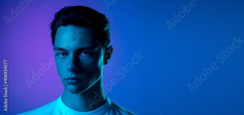 Night. Handsome caucasian man's portrait isolated on purple studio background in neon, monochrome. Beautiful male model. Concept of human emotions, facial expression, sales, ad, fashion and beauty