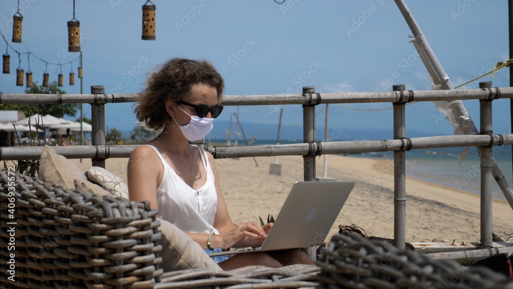 Remote working at the beach during corona virus. Female in a face mask in beach restaurant