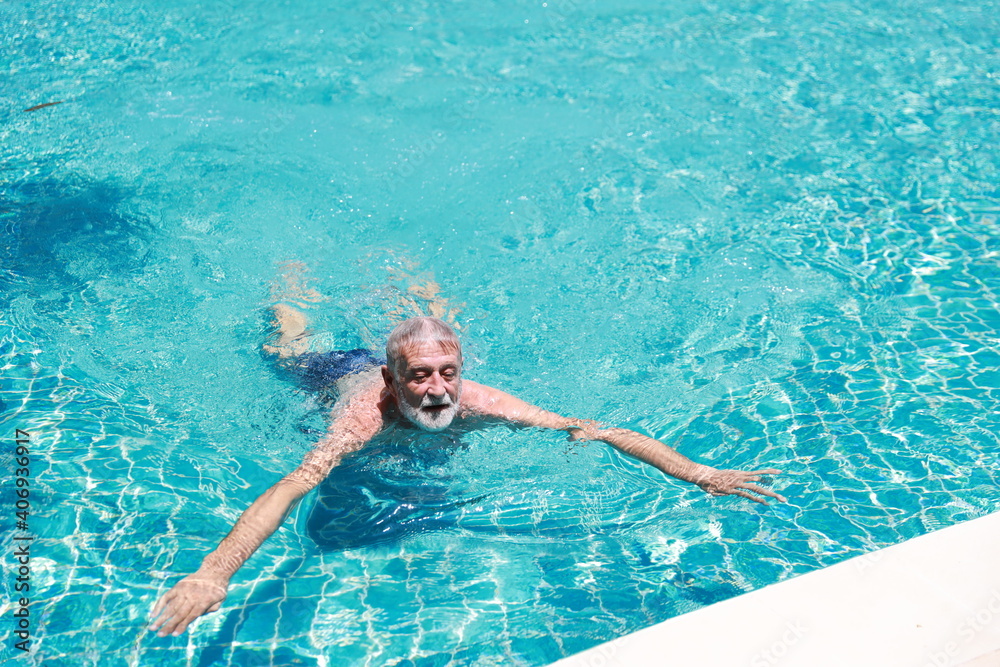 happy elderly caucasian man swimming in pool during retirement holiday with relaxation and smiling