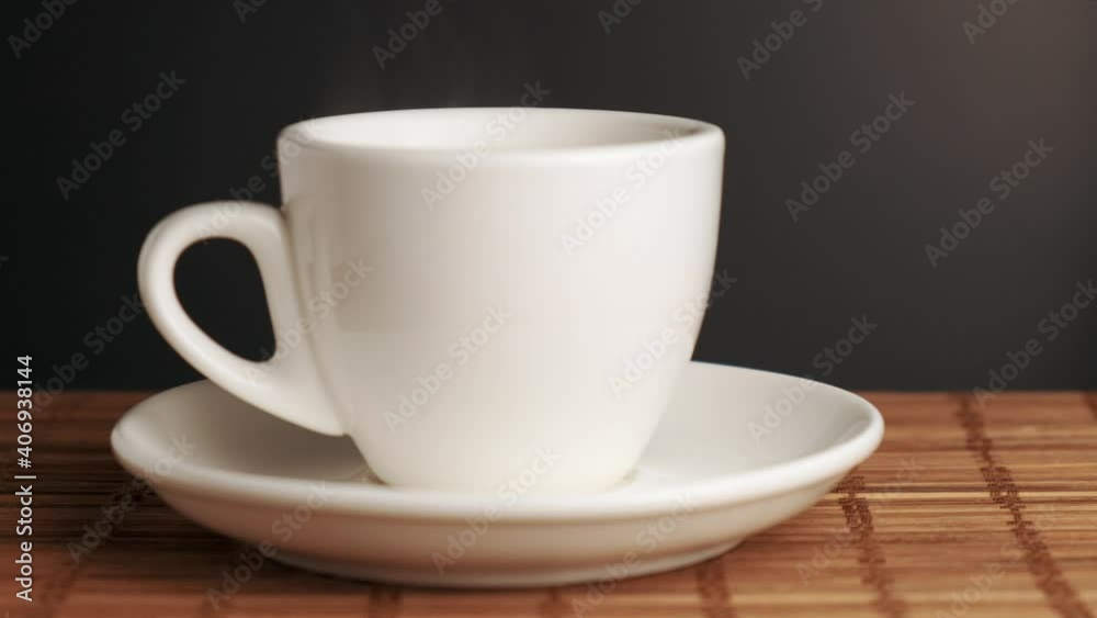 On the table is a natural bamboo mat and a white cup of coffee, there is a fragrant smoke. Black background. On the table is a natural bamboo mat and a white cup of coffee, there is a fragrant smoke. Black background.