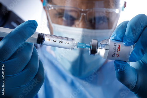 Medico con mascherina chirurgica e guanti in lattice preleva il vaccino anti-covid da una fiala di vetro,  isolato su sfondo bianco photo