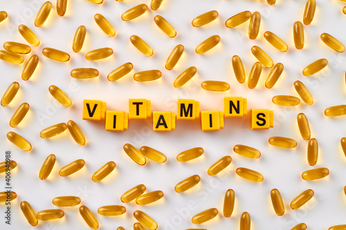 Word vitamins and yellow pills. Many capsules on white background.