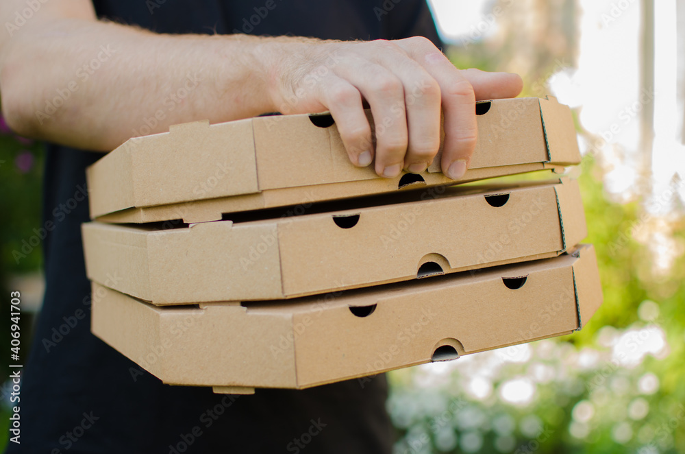 Guy giving one box, pizza delivery, guy in black t-shirt. Cropped image of a courier holding three pizza boxes isolated outdoors. Guy giving one box, pizza delivery, guy in black t-shirt. Cropped image of a courier holding three pizza boxes isolated outdoors.