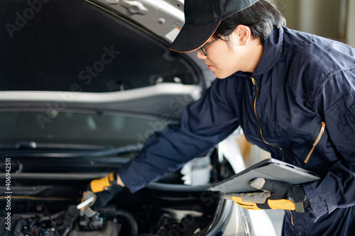 Asian auto mechanic holding digital tablet checking car engine under the hood in auto service garage. Mechanical maintenance engineer working in automotive industry. Automobile servicing and repair © zephyr_p