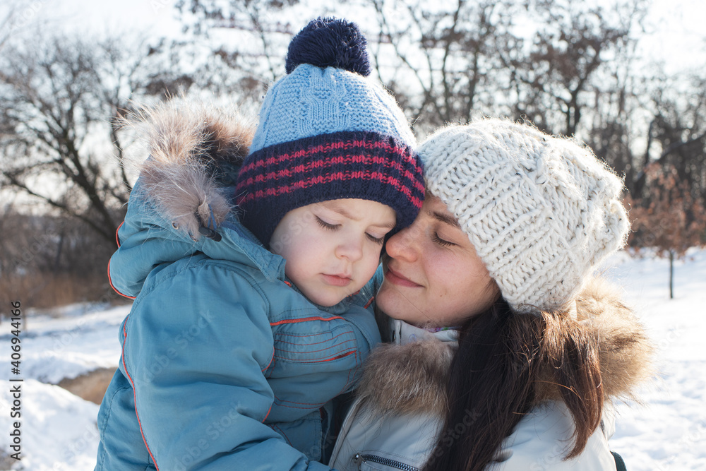 Mom and son cuddle in winter against the backdrop of nature and snow. Winter landscape and mom's love, Mother's Day. Active holidays in nature