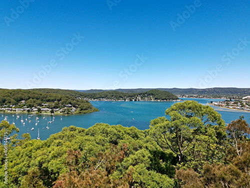 Beautiful view of a bay full of boats with tall tree in the foreground and mountains, trees and deep blue sky in the background, Allen Strom Lookout, Brisbane Water, Rocky Point Trail, New South Wales © Ivan